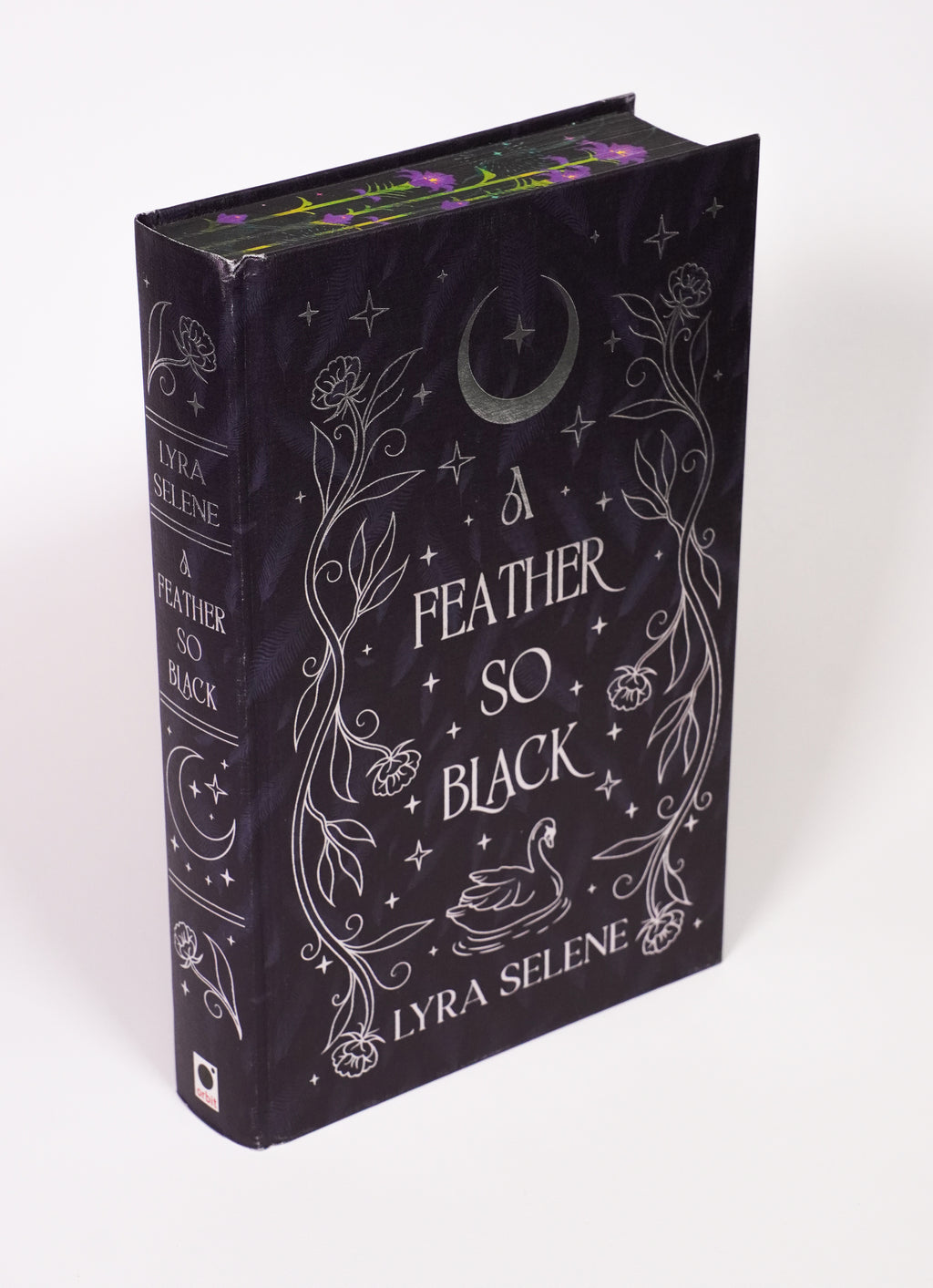 A Feather So Black FairyLoot hardcover without its dust jacket, showing bumping, creasing and rubbing at the top of the spine, edge wear, silver foil artwork and floral page edges.