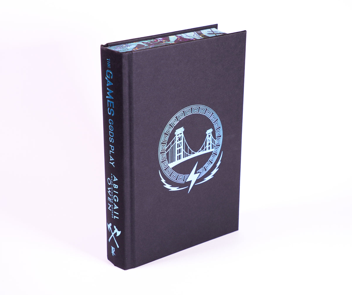 The Games Gods Play hardcover without its jacket, showing the blue foil bridge design and spine